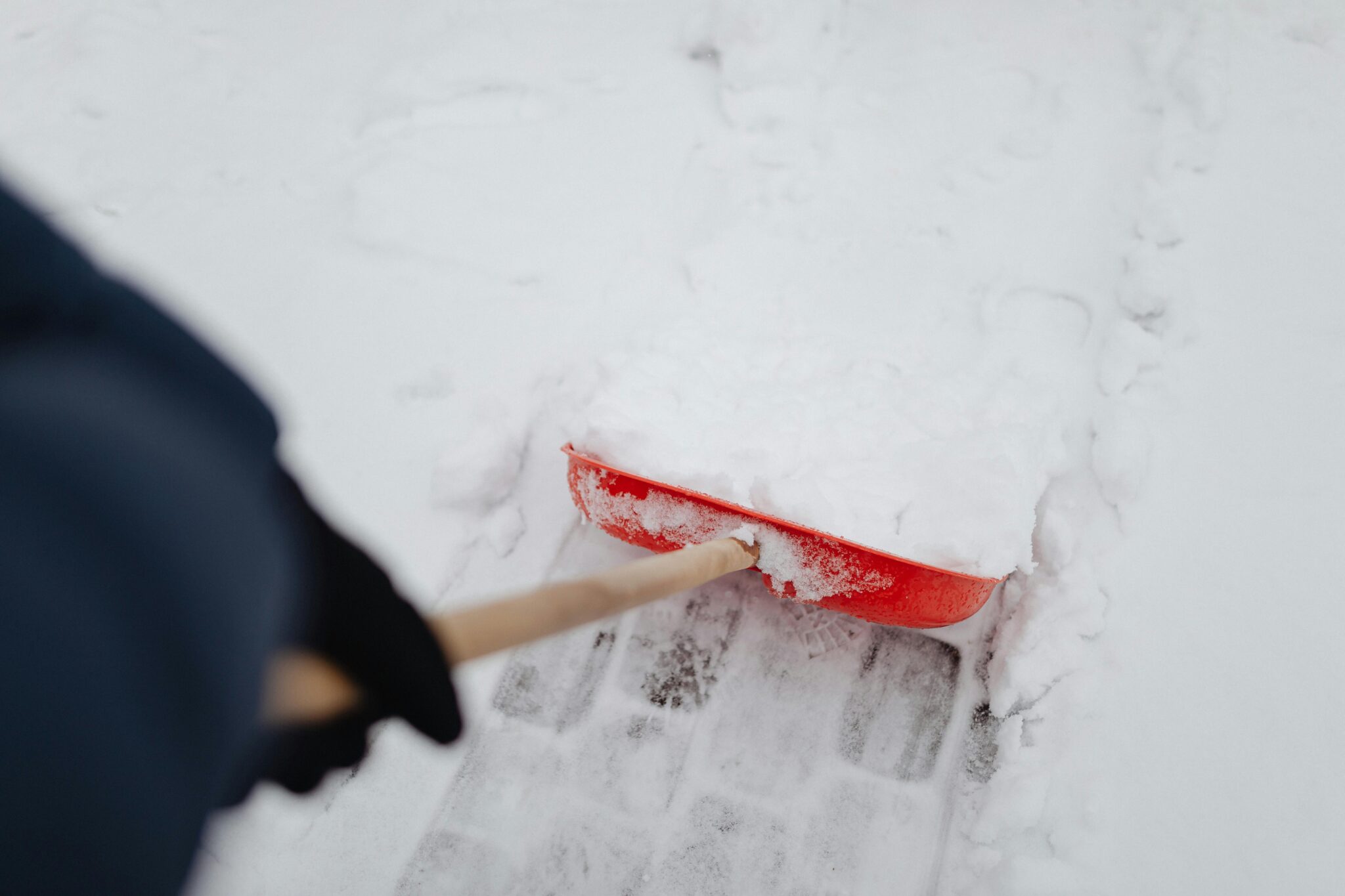 A person shoveling snow with a red shovel on a snowy day outdoors.